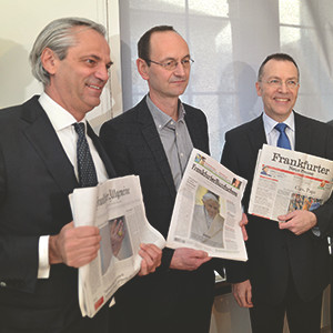 Foto: Drei Männer, die lächelnd jeweils eine Zeitungsausgabe halten