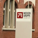 Foto: Hauseingang mit einem Aufsteller der Mediengruppe Frankfurt