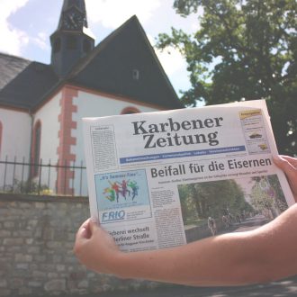 Foto: Eine Person hält eine Ausgabe der Karbener Zeitung in die Kamera