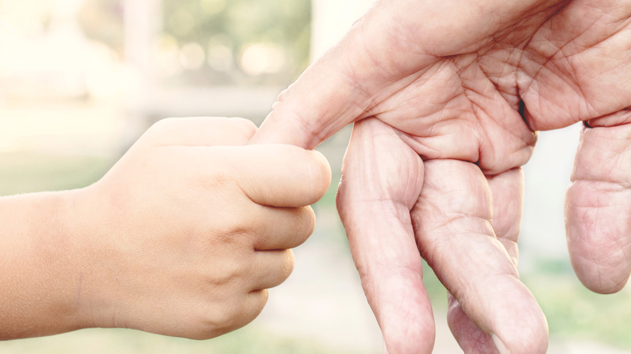 Imagebild: Eine kleine Kinderhand hält die Hand einer alten Person.
