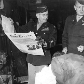 Foto: Auf dem Bild sieht man, wie der Leiter des amerikanischen Nachrichtenkontrollamtes eine frisch gedruckte Zeitung betrachtet.