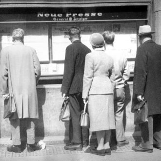 Foto: Auf dem Bild sieht man Passanten, die die Zeitungsaushänge vor dem Büro in der Schillerstraße lesen.