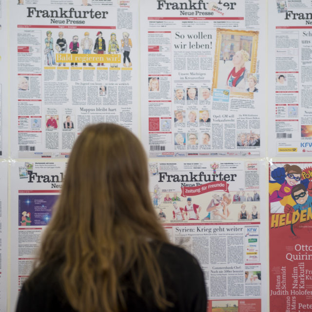 Ein Mädchen steht vor einer Wand mit aufgeklebten Titelseiten der letzten Junge Zeitung Ausgaben