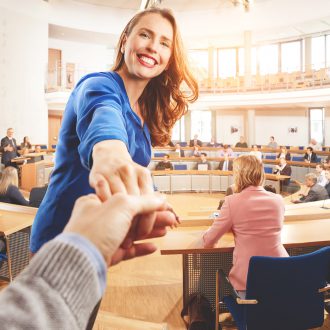 Foto: Frau in einem Konferenzsaal reicht jemandem die Hand