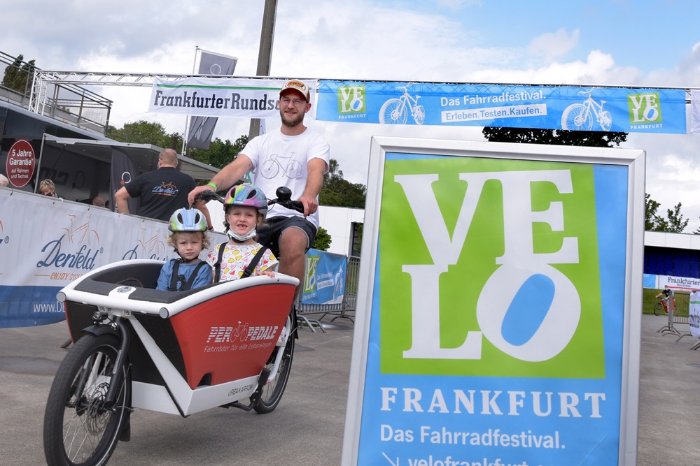 Foto: Velo Aufsteller und ein Mann mit Lastenfahrrad mit zwei Kindern vorne drin