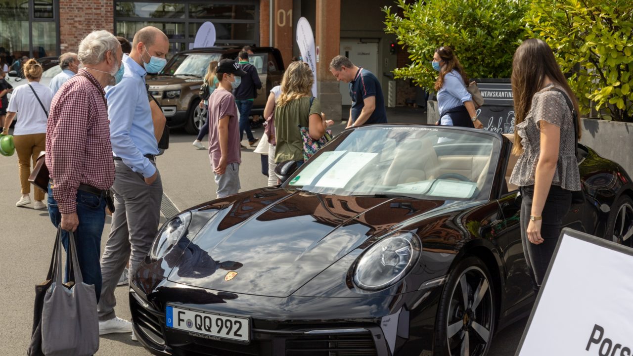 Ein älterer und ein jüngerer Mann mit Masken begutachten ein schwarzes Porsche Cabrio während der Frankfurter Automobilausstellung 2021