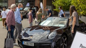 Ein älterer und ein jüngerer Mann mit Masken begutachten ein schwarzes Porsche Cabrio während der Frankfurter Automobilausstellung 2021